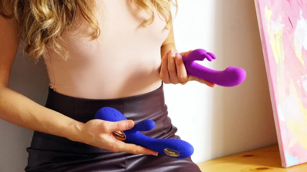 Mulher segurando dois tipos de vibradores, um em cada mão.