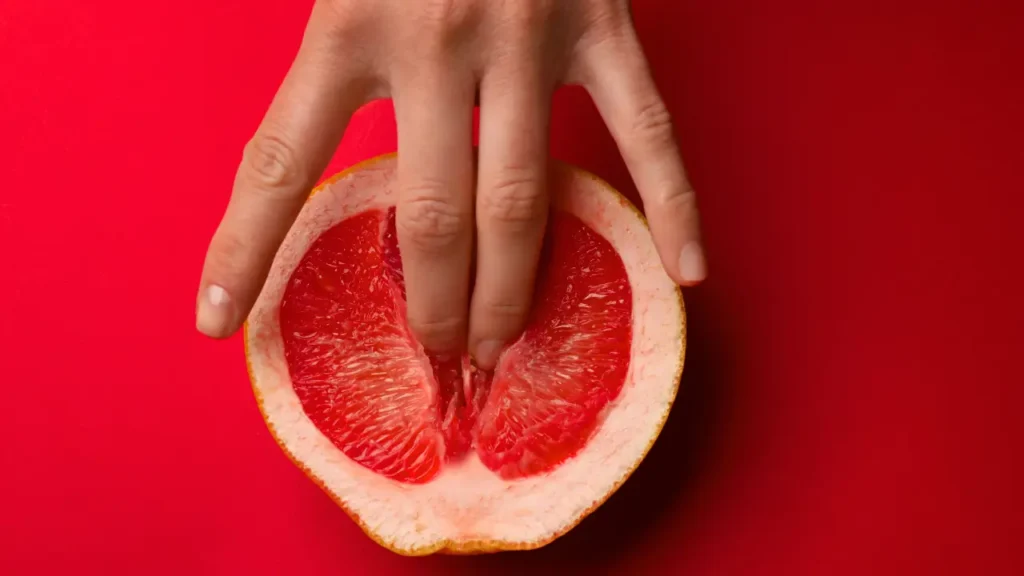 Mão penetrando uma laranja com os dedos, remetendo à masturbação feminina.